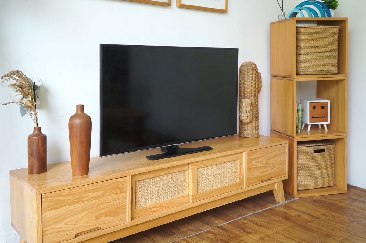 Cozy living room setup featuring a flat-screen TV on a wooden cabinet with rattan details and minimalist decor