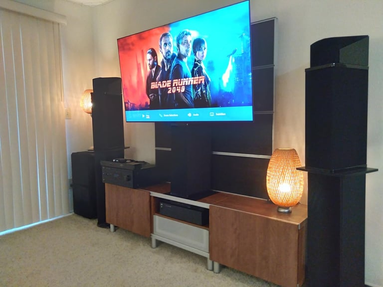 Home entertainment system with flat screen TV displaying a movie, surrounded by black speakers and wooden media console with ambient lighting