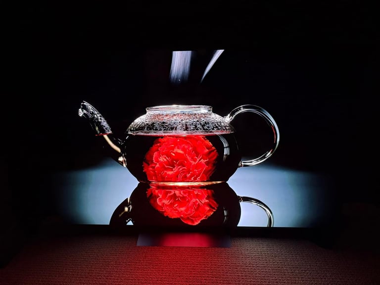 Glass teapot with red flowering tea bloom steeping against dark background with dramatic lighting