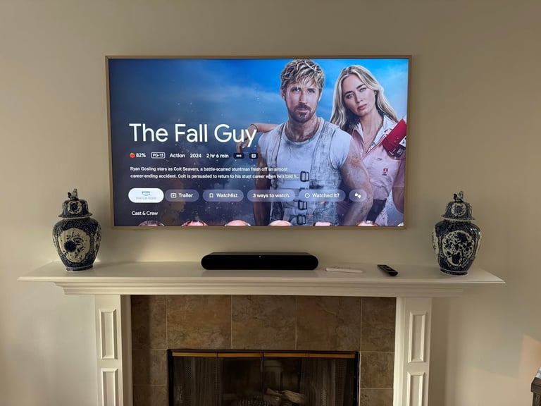 TV mounted above fireplace mantle displaying The Fall Guy streaming interface with decorative urns on either side