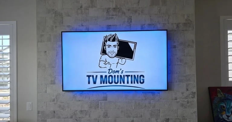 Flat-screen TV mounted on tiled wall displaying Dons TV Mounting logo with blue LED backlighting