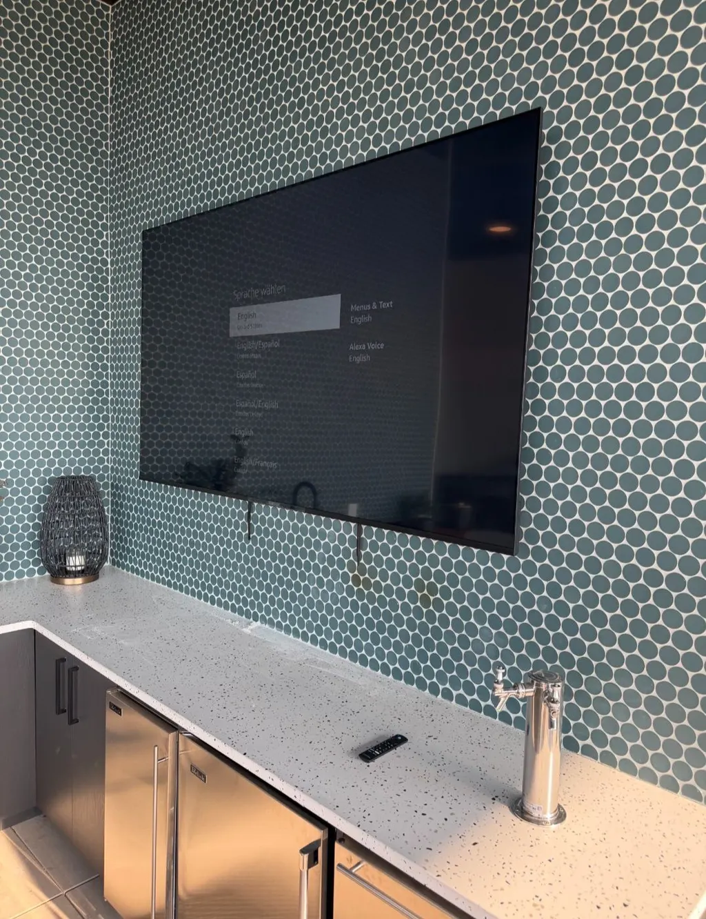 TV mounted on a wall of teal tile above a bar counter