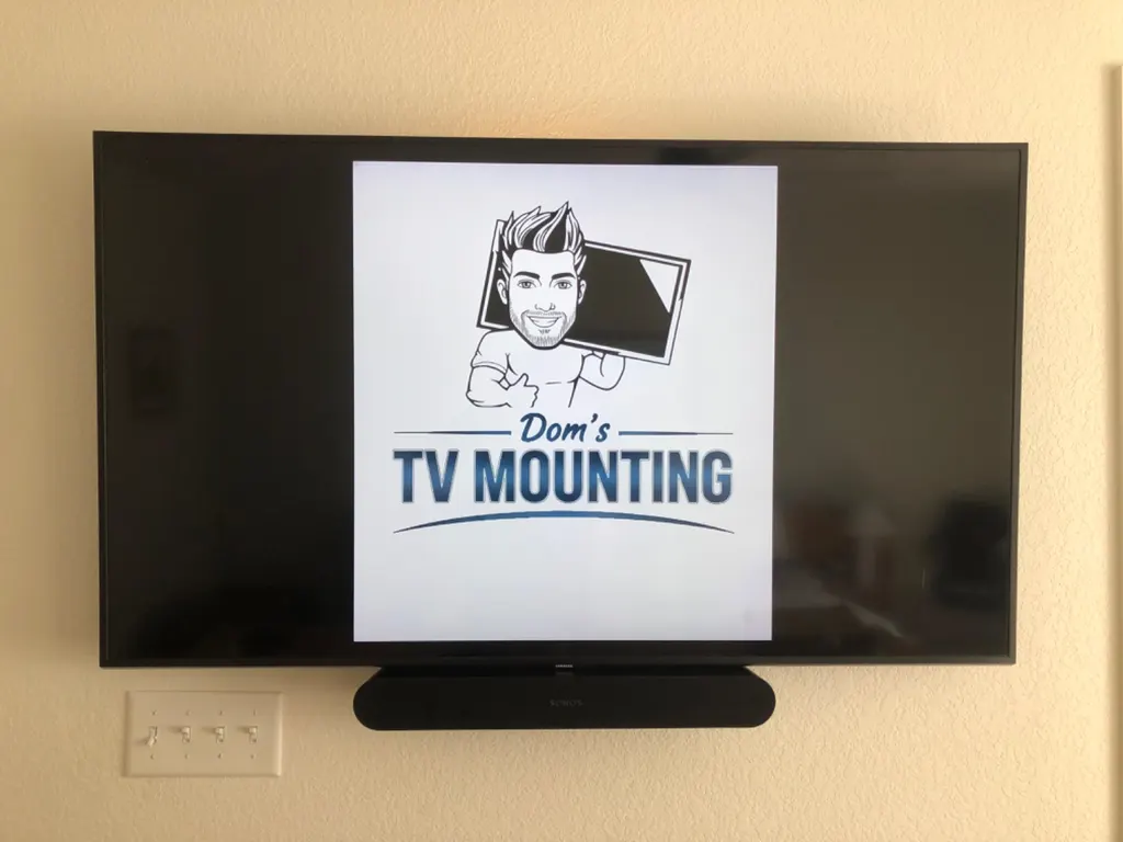 Wall-mounted TV with a soundbar below it and the Dom's TV Mounting logo on screen