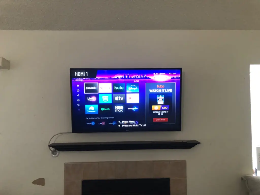 Roku TV mounted above a fireplace mantel showing streaming apps