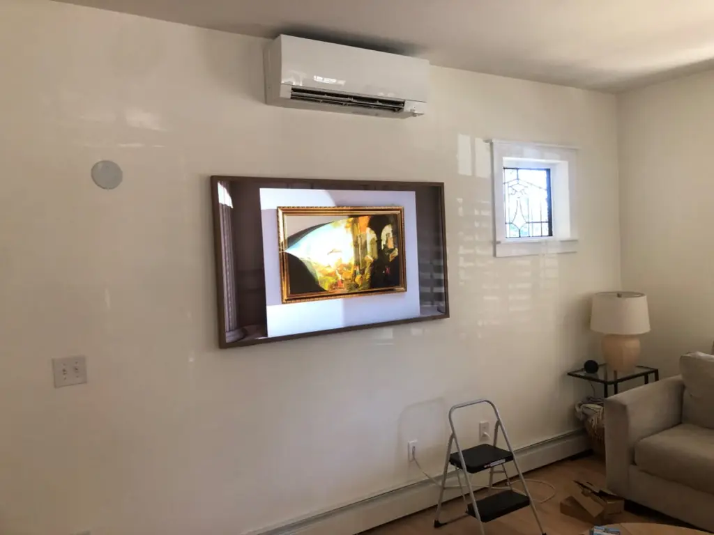 Samsung Frame TV with a dark wood bezel displaying a classic painting, wall mounted in a bright living room