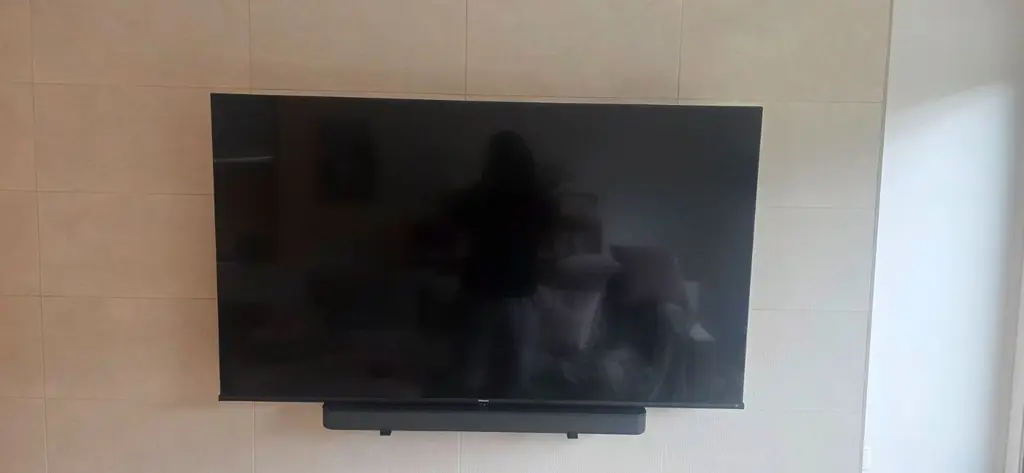 Large flat-screen TV mounted on a light tiled wall with a soundbar mounted directly below it