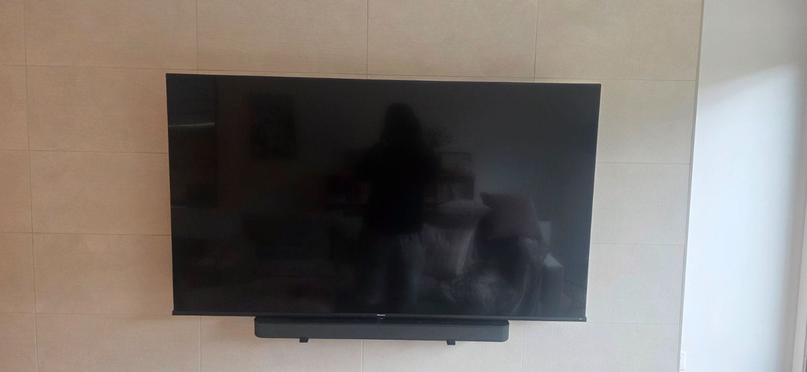 Large flat-screen TV mounted on a light tiled wall with a soundbar mounted directly below it