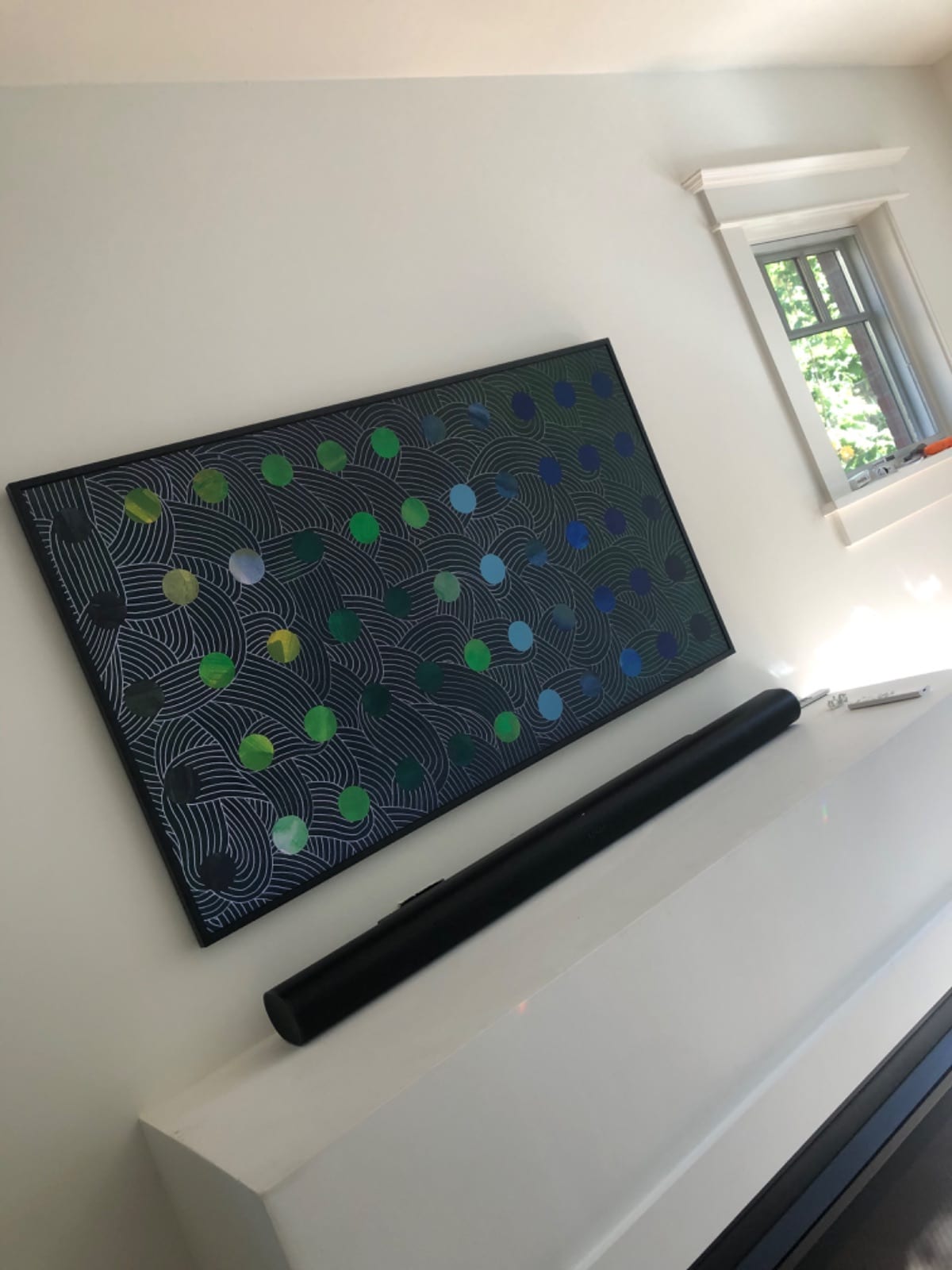 Slim TV displaying abstract art on a white wall, with a black soundbar resting on the ledge below it