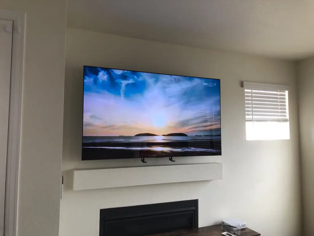 Flat screen TV mounted above a white fireplace mantel with wires hidden