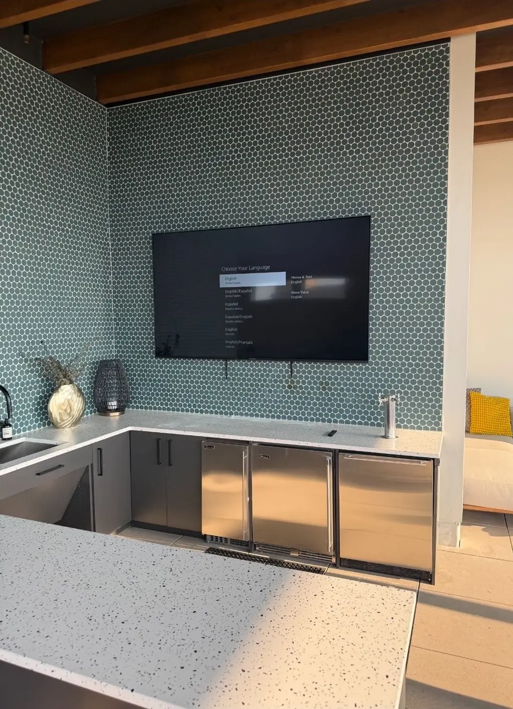 TV mounted on a hexagon tile wall above a bar counter with stainless coolers