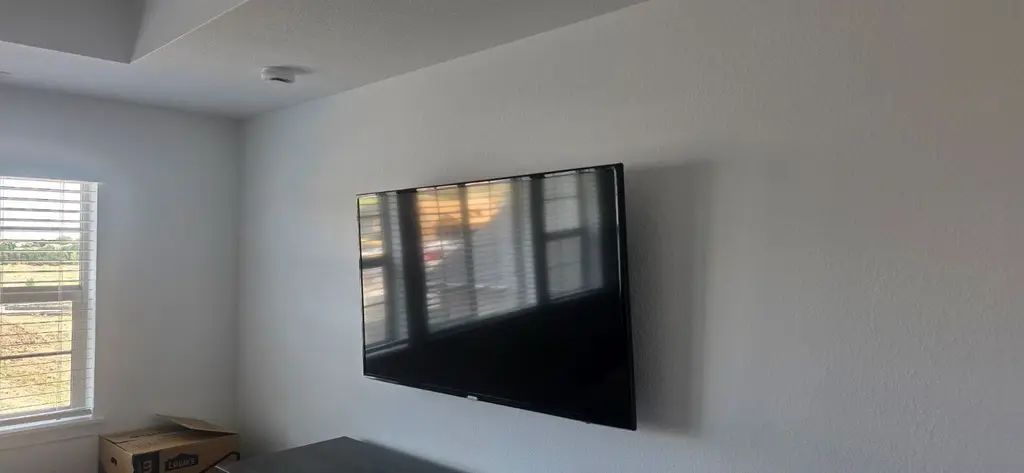 TV securely mounted on a textured wall beside a window
