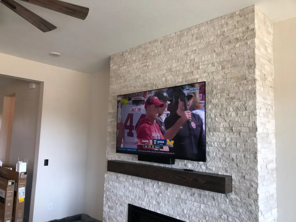 TV and soundbar mounted on a stacked stone fireplace above a wood mantel in an Aurora, CO home