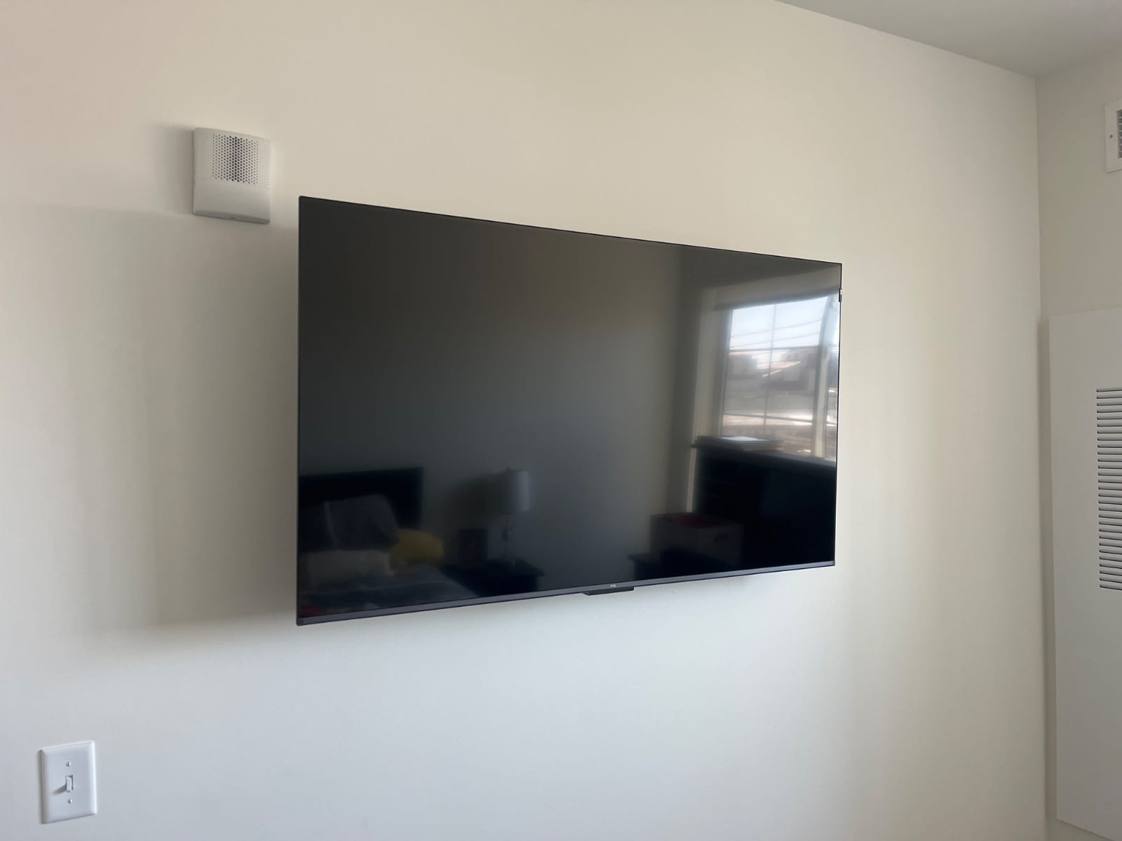 Flat-screen TV mounted on a plain cream wall with a window reflected in the screen