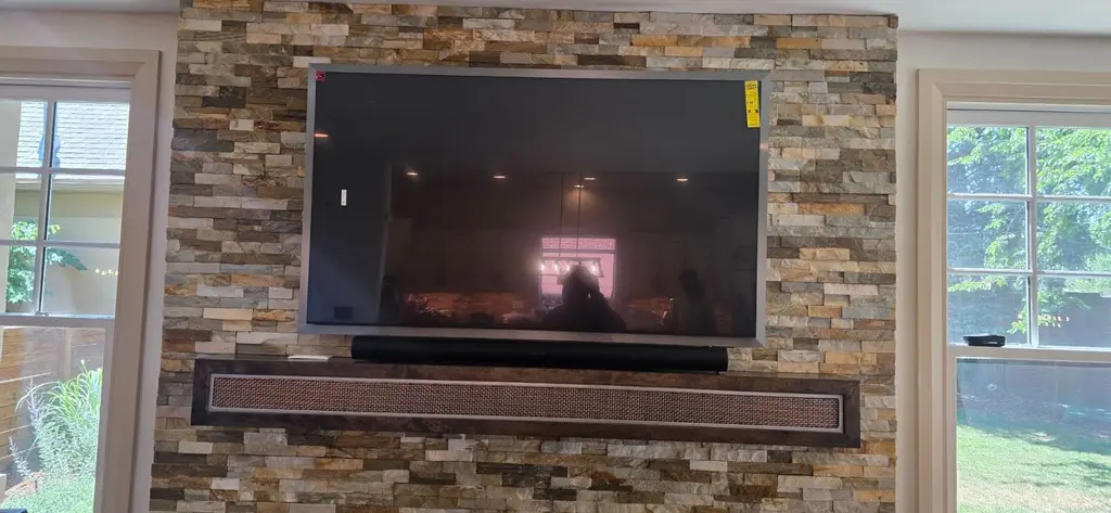 TV and soundbar mounted on a ledgestone wall between two windows in Aurora