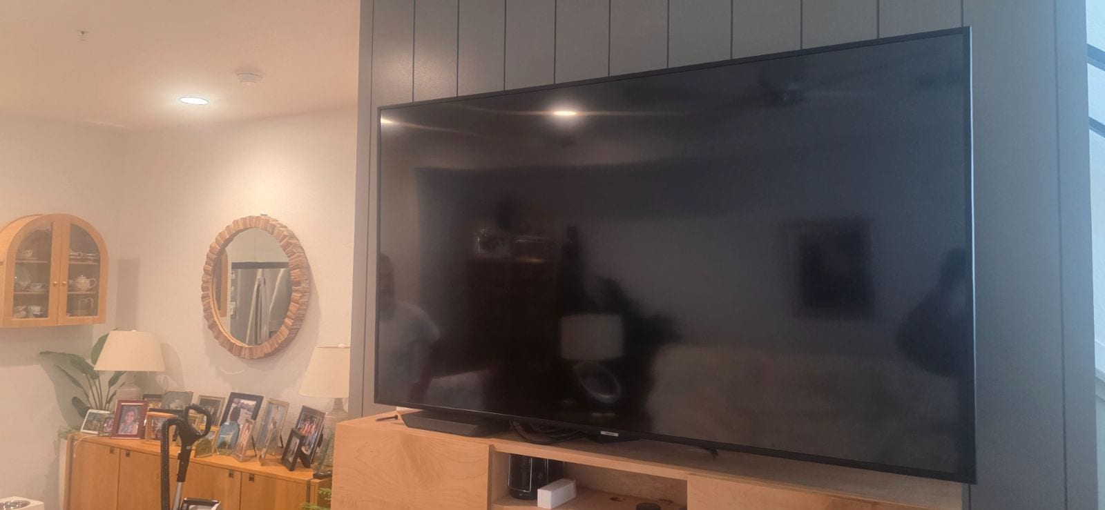 Wide flat-screen TV mounted on a dark gray shiplap wall above a light wood media console